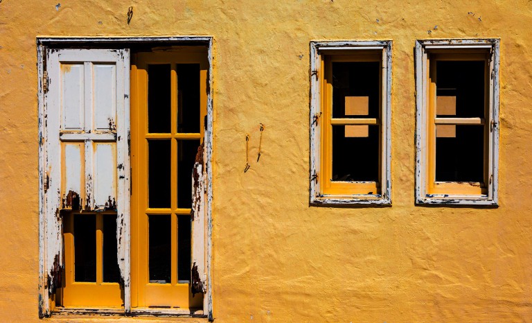 White shutters and an open window in a yellow facade.