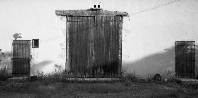 A tall wooden gate in a white wall, with deep shadows.