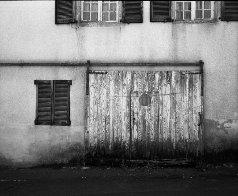 A weathered wooden garage door beneath closed window shutters.
