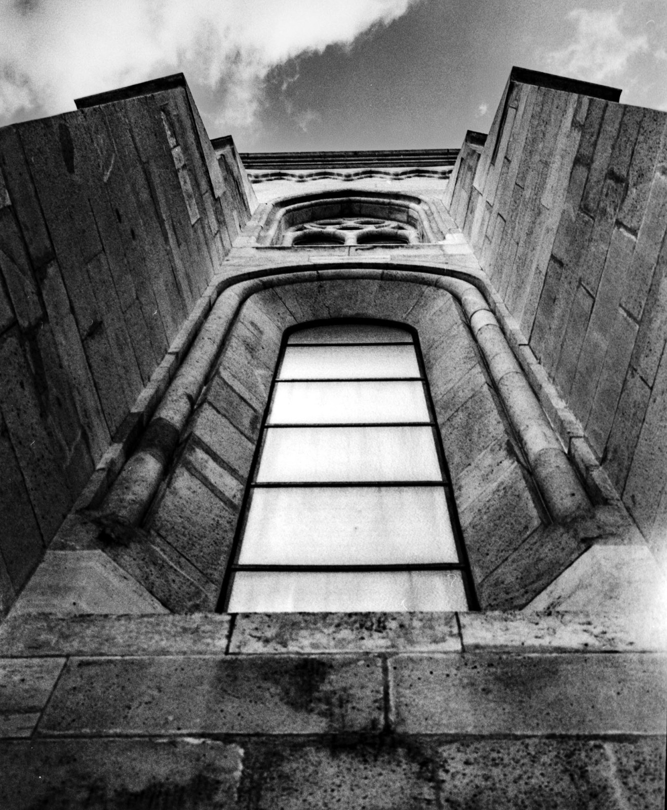 A window seen from below between converging stone walls.