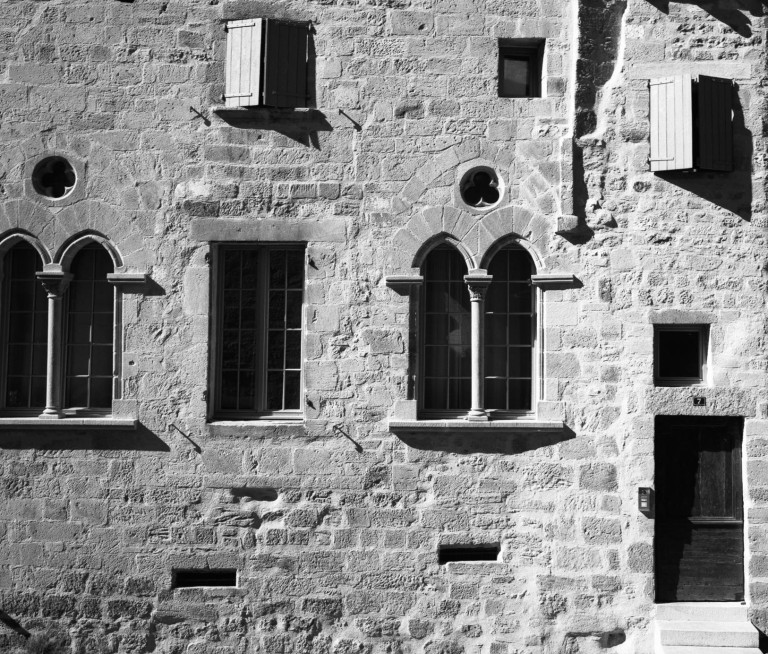 Windows and arches in the textured facade of a stone building.