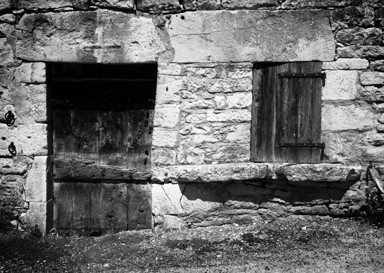 A dark rectangular opening and a wooden shutter in a worn stone wall.